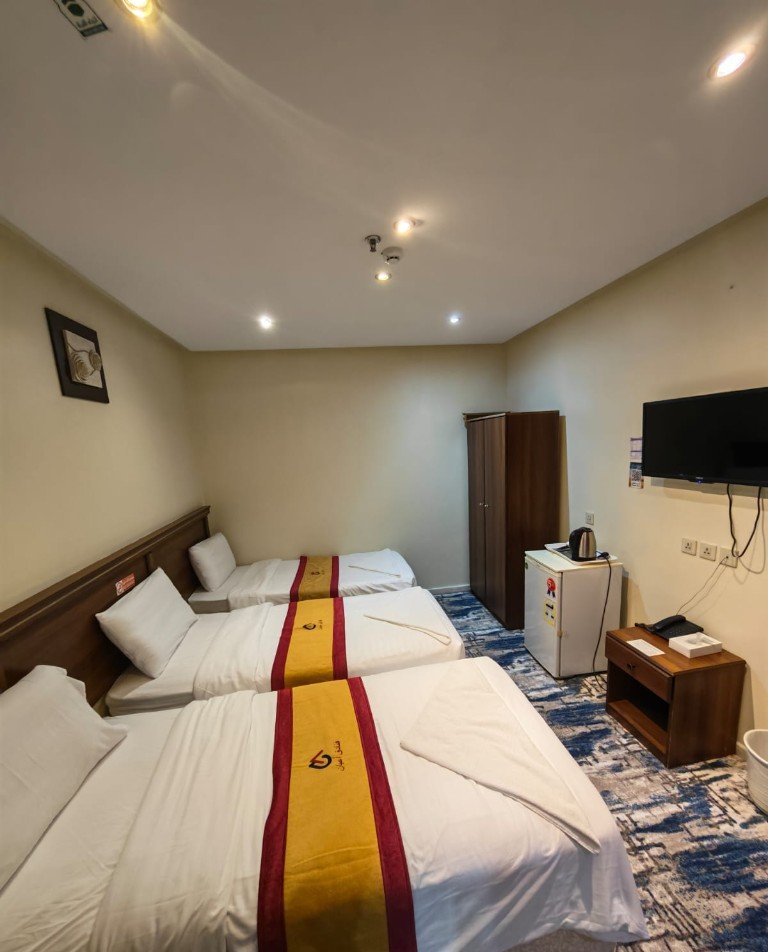 Guest room with three single beds, a television, and a small refrigerator